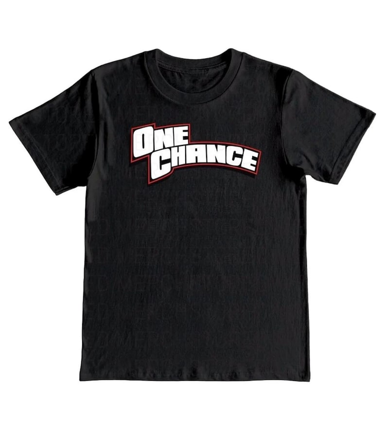 May include: Black t-shirt with the text "ONE CHANCE" in white letters with a red outline. The shirt has a crew neck and short sleeves. The text is arched across the chest.
