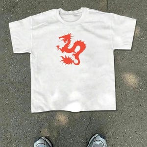 May include: White t-shirt featuring a vibrant red dragon graphic. The dragon design is centered on the front of the shirt. The shirt is made of a soft, comfortable material, perfect for casual wear.