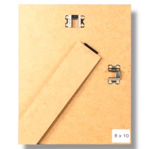 May include: Rear view of a wooden picture frame, featuring metal clips and a kickstand. The frame is light brown. Dimensions are 8 x 10 inches (approx. 20 x 25 cm).