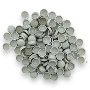 May include: A pile of light gray plastic caps with a circular design on the top surface. The caps are scattered on a white background, with some stacked and others lying flat. The caps appear to be new and unused.