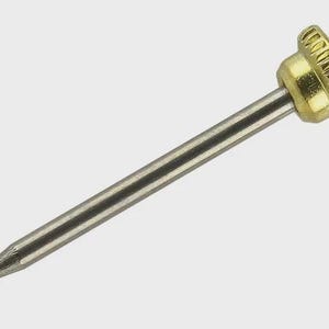 Puede incluir: Primer plano de una herramienta metálica con un eje plateado y una cabeza dorada texturizada. La herramienta tiene una punta. El fondo es de color gris claro sólido.