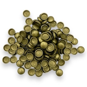 May include: A collection of small, metallic gold-coloured caps with a circular design on the top. The caps are scattered on a white background. The text "106 OPUL" is visible on the top of the caps.