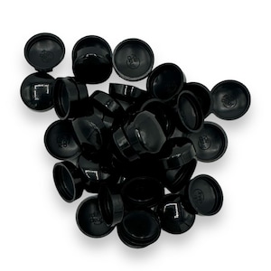 May include: A collection of glossy black plastic jar lids. Each lid has a rounded top and a flat base, with a small circular design on the top. The lids are scattered on a white background.