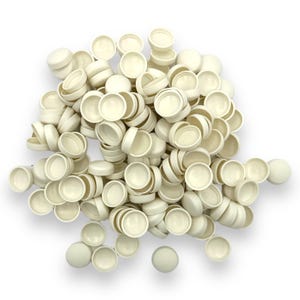 May include: A pile of off-white, round plastic caps, some with a concave interior, are scattered across a white surface. The caps are of varying sizes and are stacked on top of each other. The image is well-lit, highlighting the texture and shape of the caps.