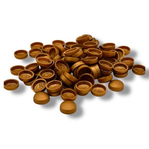 May include: A pile of small, metallic gold-colored objects, possibly caps or plugs, are scattered across a white background. The objects have a rounded, disc-like shape with a slightly raised edge. Some have visible markings.