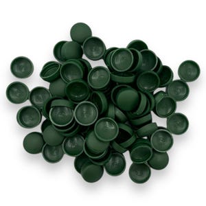 May include: A collection of dark green plastic bottle caps, some with lids on and some off, are scattered on a white backdrop. The caps are round with a slightly domed top and a circular indentation on the inside. The caps are all the same size.