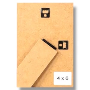 May include: Back of a rectangular picture frame with a light brown wooden backing. The frame has two black metal hangers and a fold-out stand. The label on the bottom right corner reads "4 x 6".