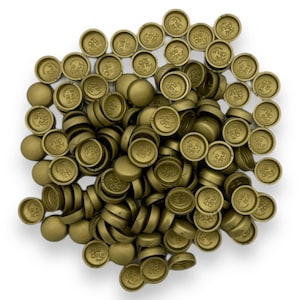 May include: A pile of gold-colored automotive parts, likely freeze plugs or similar components, are scattered on a white surface. Each part has a circular design with embossed text, suggesting branding or specifications. The parts are metallic and have a matte finish.