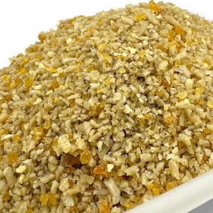 Könnte beinhalten: Nahaufnahme eines Haufens Tierfutter. Das Futter besteht aus kleinen, unregelmäßigen Stücken in Beige- und Gelbtönen. Die Textur erscheint grob und körnig. Die Beleuchtung ist hell und zeigt die Details.