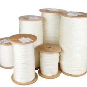 May include: A collection of white rope spools of varying sizes. The rope is neatly wound onto wooden spools. The spools are grouped together, demonstrating the different amounts of rope available. The rope has a neutral white appearance.