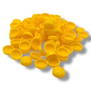 May include: A pile of bright yellow plastic caps, each with a rounded shape and a flat top. The caps are scattered across a white surface, creating a visually appealing arrangement. The caps appear to be new and unused.