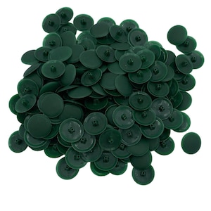 May include: A collection of dark green plastic caps, each with a circular design. The caps are disc-shaped with a raised centre and a small hole. They are scattered against a white backdrop.
