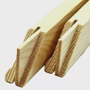 May include: Close-up of several unfinished wooden stretcher bars for canvas art. The bars are light-colored with detailed, textured edges and interlocking joints. The angled corners and notched design are visible, indicating their use in stretching and framing artwork.