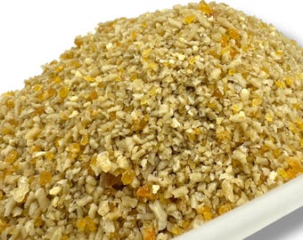 Peut inclure: Gros plan sur un tas d'aliments pour animaux, composé de petits morceaux irréguliers de couleur beige et jaune. La texture est grossière et granuleuse. L'éclairage est vif, révélant les détails.