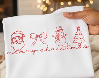 May include: White Christmas-themed towel with red line art of Santa Claus, a bow, a snowman, and a Christmas tree. The words "merry christmas" are written in red script below the illustrations. The towel is held up in front of a fireplace.