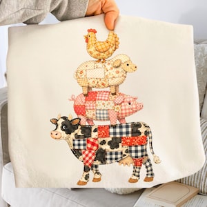 May include: A cream tote bag with a charming illustration of farm animals stacked. The cow, pig, sheep, and chicken are decorated with patchwork patterns in various colours, creating a rustic design. A delightful and unique accessory.