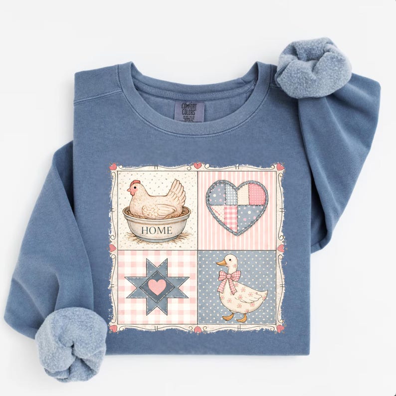 Puede incluir: Una sudadera azul de manga larga con un gr&aacute;fico que presenta una gallina en un cuenco, un coraz&oacute;n, una estrella y un pato. El gr&aacute;fico tiene un tema de granja con acentos rosas y azules. La sudadera tiene un ajuste c&oacute;modo y relajado.
