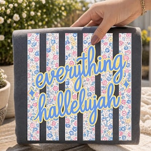 May include: A dark gray square with vertical black stripes and a floral pattern. The words "everything hallelujah" are written in blue script with a yellow outline. The floral pattern includes pink, blue, and yellow flowers.