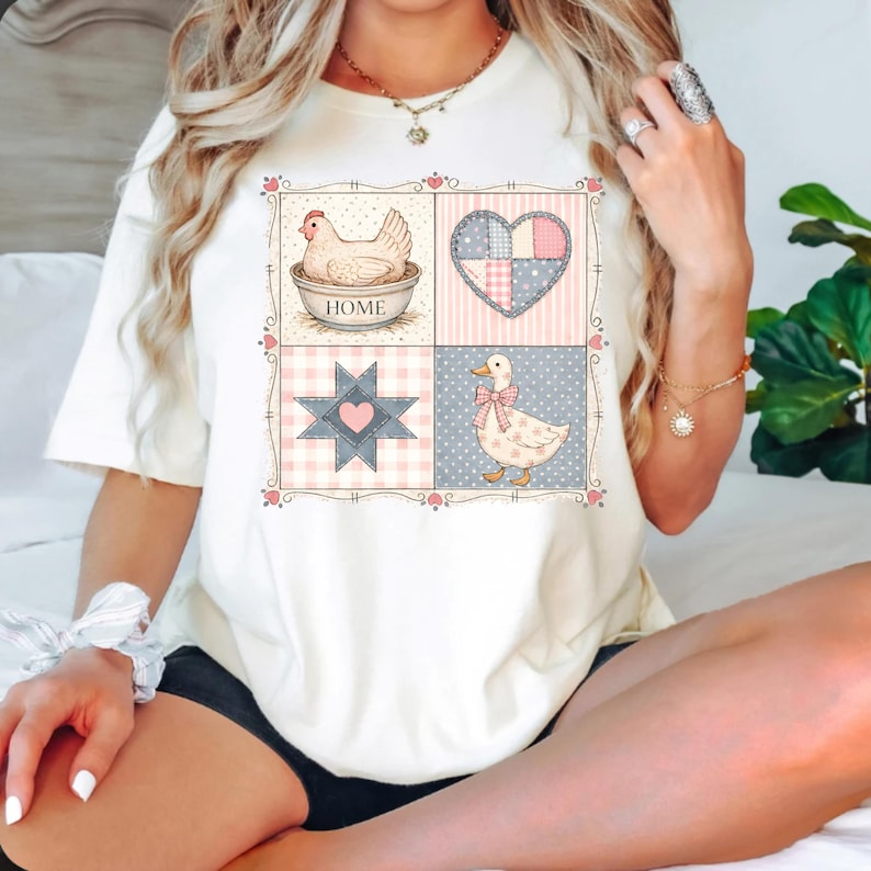 Puede incluir: Camiseta color crema con dise&ntilde;o patchwork que muestra una gallina, un coraz&oacute;n, una estrella y un pato. La palabra "HOME" est&aacute; en el cuenco. El dise&ntilde;o est&aacute; enmarcado con detalles florales rosas. La camiseta es de color neutro.