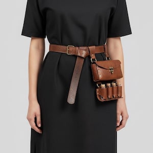 May include: A brown leather belt with a matching pouch and small vials attached. The belt is worn around the waist and has a buckle closure. The pouch has a flap closure. The vials are held in a small holder.