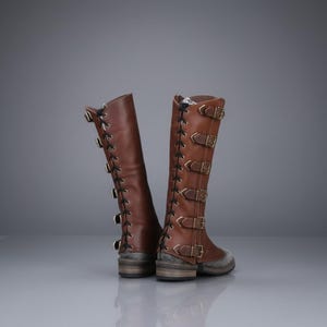 May include: Knee-high brown leather boots with multiple buckles and laces. The boots have a vintage, steampunk aesthetic, with a sturdy sole and a mix of textures and hardware.