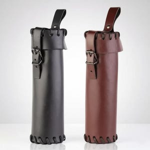 May include: Two leather quivers, one black and one brown, are displayed. Each quiver has a cylindrical shape with a buckle closure and a handle. The edges are stitched, and the leather has a smooth finish. The quivers are designed to hold arrows.