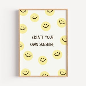 Könnte beinhalten: Ein gerahmter Wandkunstdruck mit weißem Hintergrund, einem sich wiederholenden Muster aus gelben Smileys und dem zentrierten schwarzen Text CREATE YOUR OWN SUNSHINE. Der Rahmen besteht aus hellem Holz mit einem dünnen, schlichten Profil.
