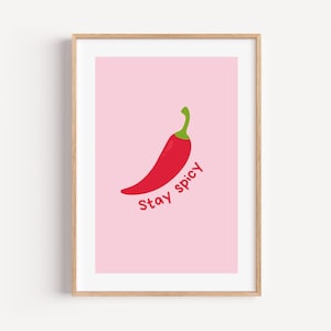 Könnte beinhalten: Ein gerahmter Kunstdruck mit einer leuchtend roten Chilischote mit grünem Stiel, zentriert auf einem hellrosa Hintergrund. Unter der Chilischote ist der Text "Stay spicy" in einer passenden roten Schrift gedruckt, alles in einem hellen Holzrahmen.