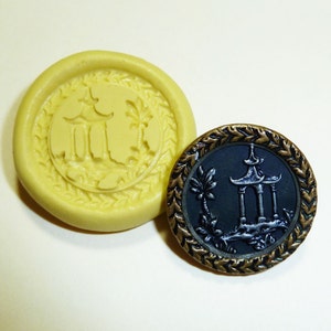 May include: A close-up of a yellow silicone mold and a black and gold button. The mold is shaped like a circle with a raised design of a pagoda in the center. The button is also circular and features a raised design of a pagoda with a palm tree in front of it.