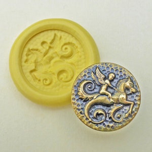 May include: A gold-toned metal button with a detailed design of a winged cherub riding a seahorse. The button has a textured surface and a blue-grey patina.