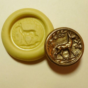 May include: A gold-colored metal button with a raised design of a deer standing in a field of grass. The button is surrounded by a decorative border of leaves.