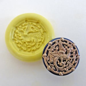 May include: A silicone mold for making resin crafts. The mold is yellow and features a detailed design of a mythical creature with wings and a tail. The mold is shown next to a finished resin piece, which is a gold-colored button with a blue background.