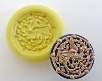 May include: A silicone mold for making resin crafts. The mold is yellow and features a detailed design of a mythical creature with wings and a tail. The mold is shown next to a finished resin piece, which is a gold-colored button with a blue background.