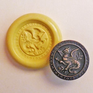 May include: A silicone mold and a metal button with a detailed design of a winged griffin holding an arrow and a branch of leaves.
