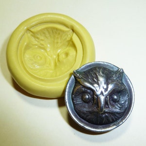 May include: A yellow silicone mold and a silver-toned owl-faced button. The mold is circular with a recessed owl face design. The button has a detailed owl face within a circular frame, showcasing intricate feather and eye details.