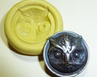 May include: A yellow silicone mold and a silver-toned owl-faced button. The mold is circular with a recessed owl face design. The button has a detailed owl face within a circular frame, showcasing intricate feather and eye details.
