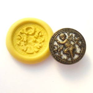 May include: A silicone mold for making resin or polymer clay jewelry. The mold features a detailed design of a cherub with wings, surrounded by floral accents. The mold is yellow and the design is in relief.