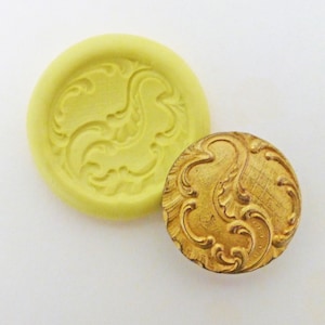 May include: A yellow silicone mold with a raised design of a swirling floral pattern. Next to the mold is a gold-colored metal button with the same swirling floral design.