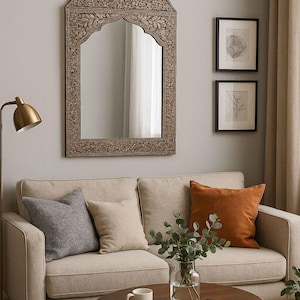 Pode incluir: Sala de estar com sofá bege, almofadas cinzentas, bege e laranja, e espelho de madeira entalhada. Mesa de centro redonda com caneca, livro e vaso. O espelho tem cerca de 100 cm de largura.