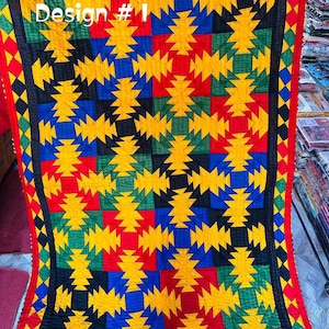 May include: A colorful textile with a geometric pattern. The design features yellow, red, blue, green, and black shapes. The text "Design # 1" is visible in the upper left corner. The edges are trimmed with red and green borders.
