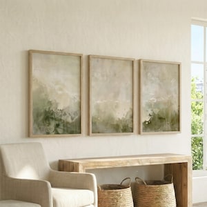 Könnte beinhalten: Ein Set aus drei rechteckigen Wandbildern mit abstrakten Aquarell-Waschungen in Salbeigrün, Creme und Beige. Jedes Bild ist in einen hellen Holzrahmen gefasst und zeigt weiche, ineinander verlaufende Farbübergänge.