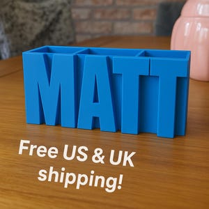 Könnte beinhalten: Ein leuchtend blauer Schreibtisch-Organizer in Form des Namens "MATT". Der Organizer hat drei Fächer und besteht aus einem soliden Material. Die fetten Buchstaben heben sich von der Holzoberfläche ab. Modernes und funktionales Design.