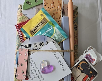 May include: A collection of items wrapped in floral paper, tied with twine. Includes a green clip, tea, stickers, a pen, and a card that says "A Pocket Hug". A purple heart-shaped charm is attached.