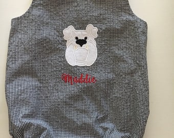 May include: A black and white gingham baby romper with a bulldog applique. The romper has red buttons on the straps and the name "Maddie" embroidered in red. The bottom has a ruffled hem.