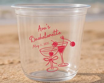 May include: A clear plastic cup featuring red printed text that reads Ava's Bachelorette May 7, 2026. The design includes two illustrated cocktail glasses with cherries and a bow detail, all rendered in a consistent red line art style.