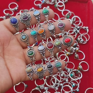 Peut inclure: Une collection de bagues en argent ornées de pierres précieuses variées, dont du lapis-lazuli bleu, de l'améthyste et de la malachite verte. Les bagues présentent des motifs détaillés et sont présentées sur un fond rouge. Les pierres sont ovales et rondes.
