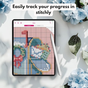 May include: A digital cross-stitch pattern displayed on a tablet, featuring a mailbox design with pink, blue, and red elements. The screen shows the text "Done" and "Overview". A white stylus rests on the screen. The text "Easily track your progress in stitchly" is at the top.