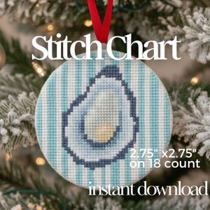 Puede incluir: Adorno redondo cosido con un fondo a rayas azules y blancas y un diseño de ostra. El adorno mide 7 cm x 7 cm y tiene las palabras "Stitch Chart" e "instant download". Se adjunta una cinta roja para colgarlo.