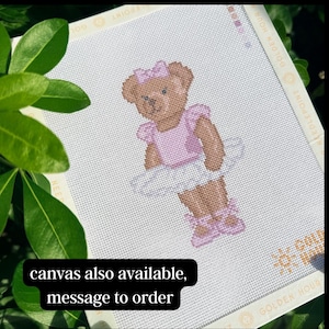 Puede incluir: Un lienzo de punto de aguja con un oso de peluche marr&oacute;n que lleva un maillot rosa claro, un tut&uacute; blanco, un lazo rosa a juego y zapatillas de ballet rosas. El borde del lienzo incluye el texto GOLDEN HOUR NEEDLEPOINT en un patr&oacute;n.
