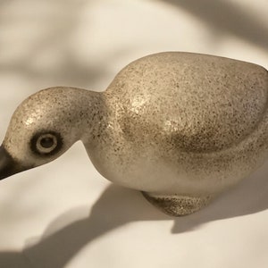May include: A ceramic bird figurine with a speckled gray and brown finish. The bird has a small black beak and a single black eye.